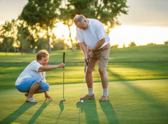 active senior lifestyle, elderly couple playing golf together at sunset on putting green.
