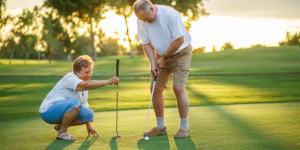 active senior lifestyle, elderly couple playing golf together at sunset on putting green.